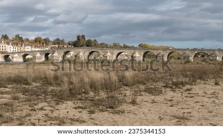 Looking across a sandy dry riverbed at a bridge across dried out plants