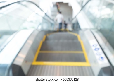 Looking along a descending escalator, with objects around the escalator motion blurred. An unrecognisable silhouette of a person stands at the bottom of the escalator.