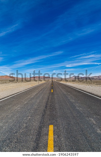 Looking along a long, straight road through\
the Nevada desert, with a blue sky\
overhead