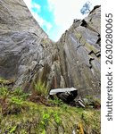 Looking up between two converging slate walls in Dinorwic Quarry, Llanberis, North Wales. Moss and ferns below, bright blue sky above. No people.