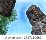 Looking up from between two large rock formations with vibrant trees on the side under a bright blue sky.