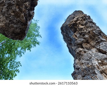Looking up from between two large rock formations with vibrant trees on the side under a bright blue sky.
