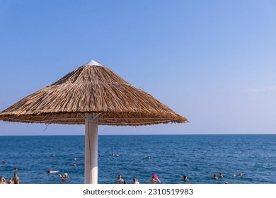 Looking at the blue sea through a straw beach umbrella.Straw umbrellas with sunbeds on the sandy beach.Bamboo umbrellas, blue sky on summer, holiday and relax concept