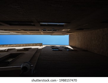 Looking Up To Blue Sky Trapped Alone Between Two Tall High Rise Buildings In Dark Alley Way.