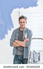 Looking at camera, a handsome grey haired man painting the living room walls of his new home