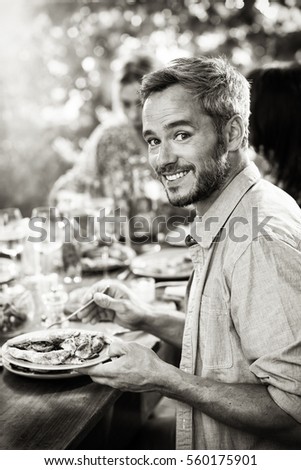 Looking at camera, portrait of an handsome man with gray hair lunching with friends on a terrace table. Black and white