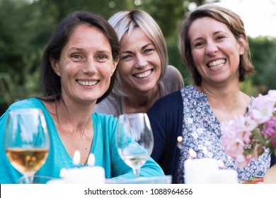 Wenn man die Kamera betrachtet, teilen sich drei Freundinnen in ihren 40ern einen Moment der Mittäterschaft. Sie versammelten sich um einen Tisch im Garten, um ein Essen mit Freunden zu teilen.