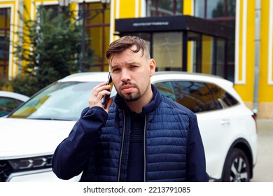 Looking At Camera Young Caucasian 34 Years Old Sad Concentrated Man With Goatee Beard Talks On Smartphone On Street Near White Car. Waist Up Lifestyle Business Portrait, Difficult Conversation