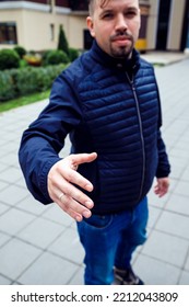 Looking At Camera Young Caucasian Businessman 34 Years Old Man With Goatee Beard Offering Handshake Palm Hand Giving As Greeting On Street. Three Quarter Length Lifestyle Portrait, Vertical Photo.