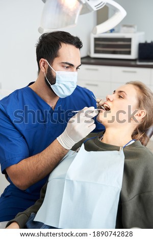 Looking carefully. Pretty female patient sitting at the clinic during examination of her teeth by skillful multirace dentist. People, medicine, stomatology and health care concept. Stock photo