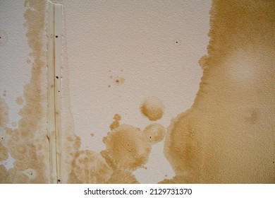 Looking up at a ceiling damaged by water, streaked and stained white sheetrock with mottled and spotted moisture stains.
