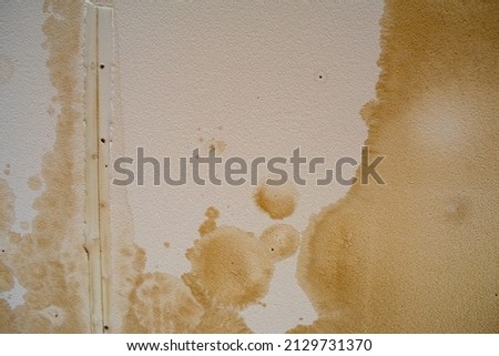 Looking up at a ceiling damaged by water, streaked and stained white sheetrock with mottled and spotted moisture stains.