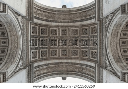 Looking up at the centre of the famous Arc de Triomphe. Detail under view of carvings under the arch of the Triumphal Arch. Iconic touristic architectural landmark of Paris, Selective focus.