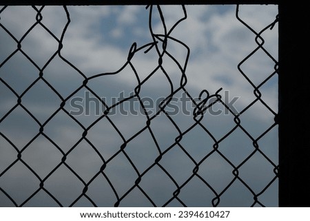 Looking up at a chain link fence with blue sky and clouds. wire fence. Chain link fence see sky. Opening in metallic fence. blue sky. Challenge. breakthrough concept.                      