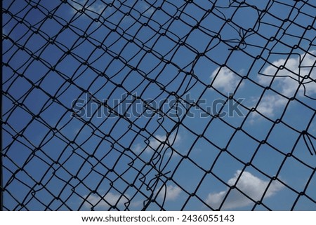 Looking up at a chain link fence with blue sky and clouds. wire fence. Chain link fence see sky. Opening in metallic fence. blue sky. Challenge. breakthrough concept
