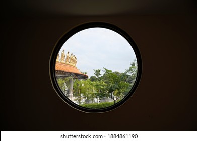 Looking from the circular window inside the building of the Chinese temple Fo Guang Shan Thaihua Temple, there are many small golden Guanyin, green trees and bright sky.