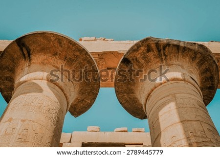 Looking up at the colossal pharaonic stone pillars and decorated lintels under a clear blue sky in Karnak Temple complex.