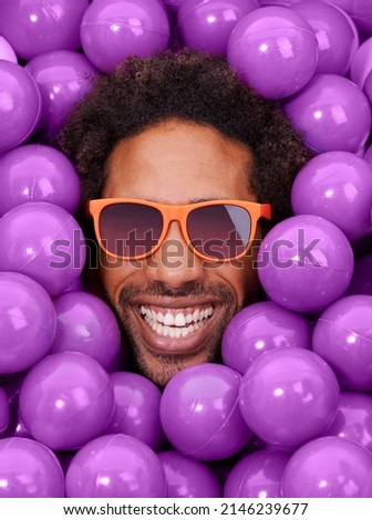 Looking cool and crazy. A young black mans face amongst purple pit balls.