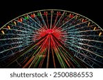 Looking up at a dazzling Ferris wheel, its lights create a vibrant display against the night sky. The colorful design and dynamic structure evoke excitement and joy, captivating all who see it.