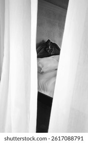 looking to a double bed through two long white net curtains, the bed has a wooden spanish style vintage head board, the bedding is white. The curtains are blowing in the wind 