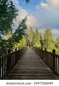 Looking down a bridge surrounded by green trees, blue sky, and river