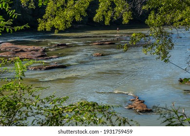 Looking down from the cliff at the Chattahoochee river in Georgia at a man standing in the shallow water fly fishing in the distance on a bright sunny day in late summer - Powered by Shutterstock