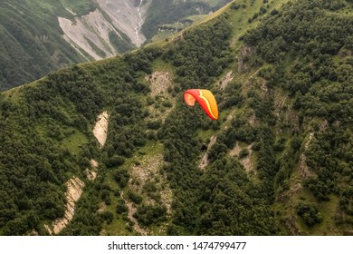 Looking Down At A Couple Hang Gliding High Over The Lower Caucasus Mountains With Cliffs And Trees And A Tiny River Running Far Below