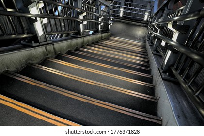 Looking down a dark concrete staircase with two bright yellow caution strips on the edge of each stair and metal railings - Powered by Shutterstock