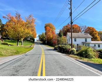 Looking down an empty, endless road that is surrounded by fall foliage and countryside homes.