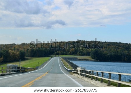 Looking down an empty, endless road that is surrounded by fall foliage and the water reservoir.