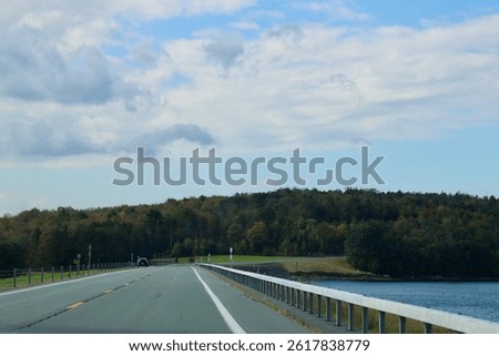 Looking down an empty, endless road that is surrounded by fall foliage and the water reservoir.