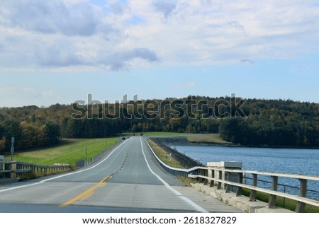 Looking down an empty, endless road that is surrounded by fall foliage and the water reservoir.