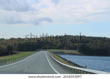 Looking down an empty, endless road that is surrounded by fall foliage and the water reservoir.
