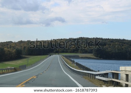 Looking down an empty, endless road that is surrounded by fall foliage and the water reservoir.