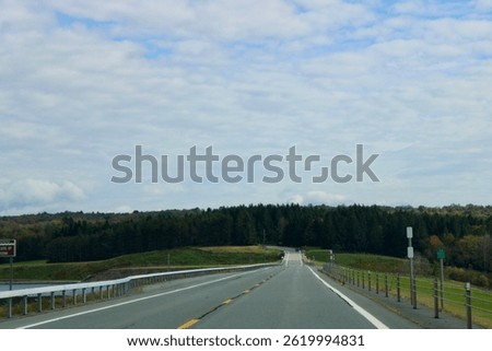 Looking down an empty, endless road that is surrounded by fall foliage and the water reservoir.