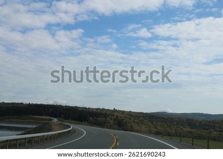Looking down an empty, endless road that is surrounded by fall foliage and the water reservoir.