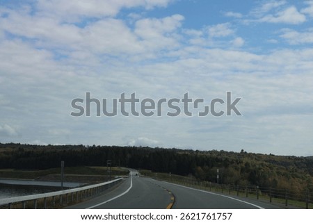 Looking down an empty, endless road that is surrounded by fall foliage and the water reservoir.