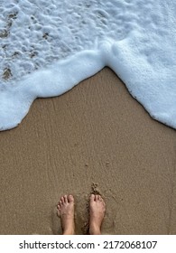 Looking Down At Feet On Sandy Beach With White Sea Foam