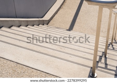 Looking down a flight of concrete staircase to a landing  with stainless steel handrail outdoors in a public space during the daytime