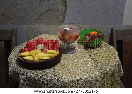 Looking down from a high center angle at a vibrant fruit cocktail glass accompanied by fresh cut watermelon and pineapple served in a traditional wooden container.