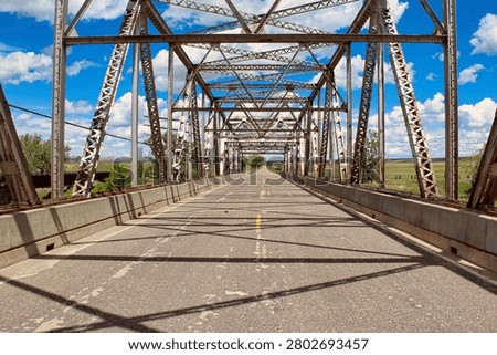Looking Down Highway 10 through the Powder River Bridge above the Powder River in Eastern Montana.

I stood in the middle of the road to take this shot. I love the beautiful sky with clouds up above the trusses and the play of shadows on the road below.

The Powder River Bridge is near the confluence of the Yellowstone River in Prairie County in Southeastern Montana. It is a steel truss style bridge built in 1946 and placed on the National Register of Historic Places in 2010. In 1946, the 633 foot long bridge served as a vital transportation link on U.S. Highway 10 and is now a frontage road to Interstate 94.
