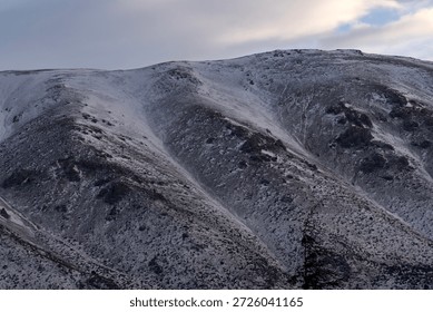 Looking down into a deep and dark valley between snowy mountain ridges under a thick layer of grey clouds showing the immense scale of the high altitude alpine wilderness territory region