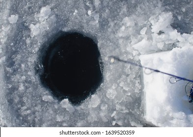 Looking Down Into The Ice Hole And The Little Line On The Ice Fishing Pole Out On The Frozen Winter Lake. 