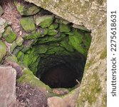 Looking down into an old abandoned hand dug well located in rural Missouri, MO, United States, US, USA.  The casing of the well is made from locally sourced rocks now covered in a bright green moss.