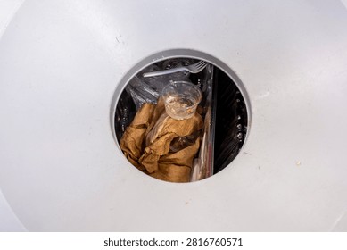 Looking down into the opening of a white trash can filled with discarded paper and plastic waste.