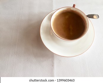 Looking down on a cup of hot coffee on a white tablecloth.