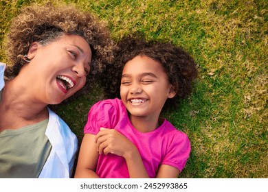 Looking Down On Grandmother With Granddaughter Lying Outdoors On Grass Looking Up At Camera - Powered by Shutterstock