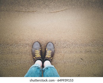 Looking down on a pair of brown leather shoes standing on a sandy ocean beach. Summer vacation concept. selective focus and toned image
