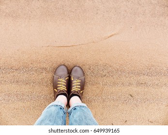 Looking down on a pair of brown leather shoes standing on a sandy ocean beach. Summer vacation concept. selective focus and toned image
