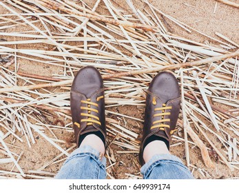 Looking down on a pair of brown leather shoes standing on a sandy ocean beach. Summer vacation concept. selective focus and toned image
